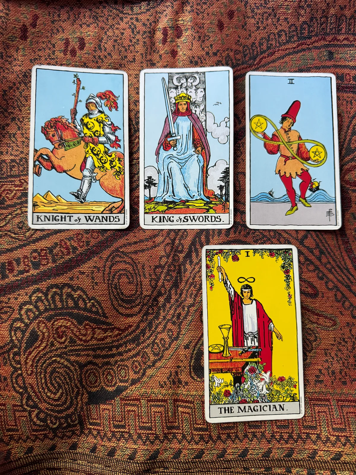 Knight of Wands, King of Swords, and Two of Pentacles above The Magician on patterned cloth.